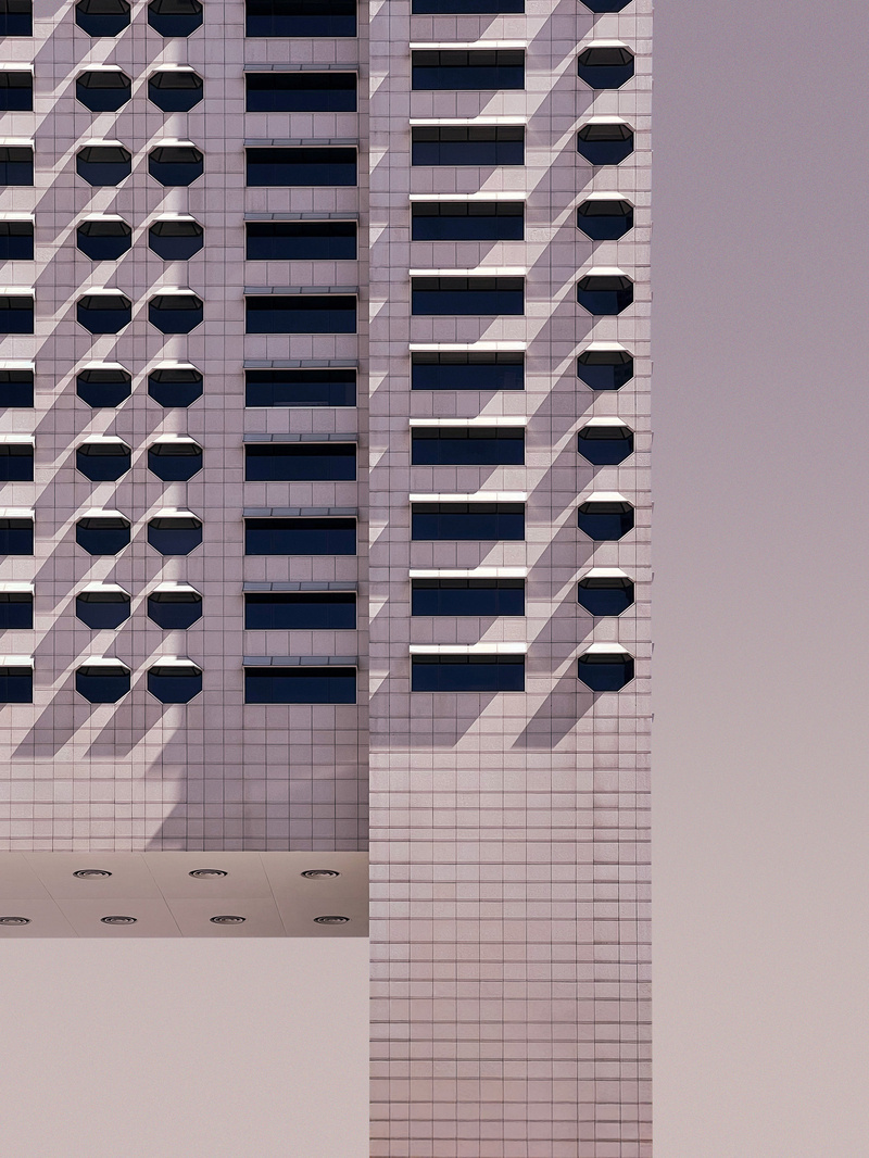 A pale pink tower shot flat against a lavender sky, its rows of dark octagonal and rectangular windows throwing hard diagonal shadows.