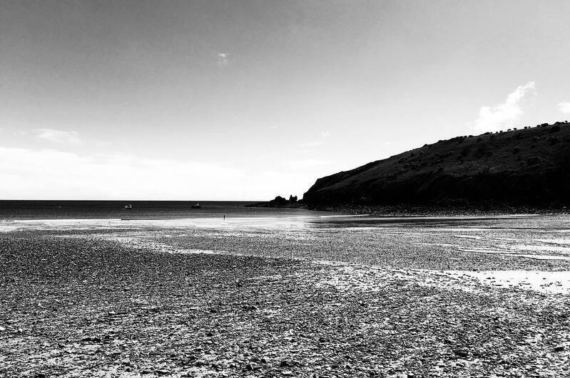 A rocky shoreline stretches out toward a calm sea with a hillside visible in the distance under a partly cloudy sky.