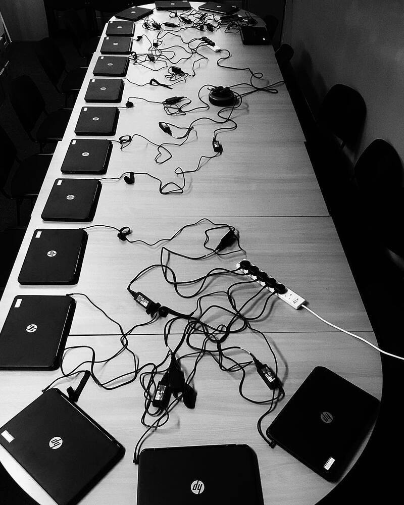A long table is filled with multiple closed HP laptops connected to numerous power cords and adapters.