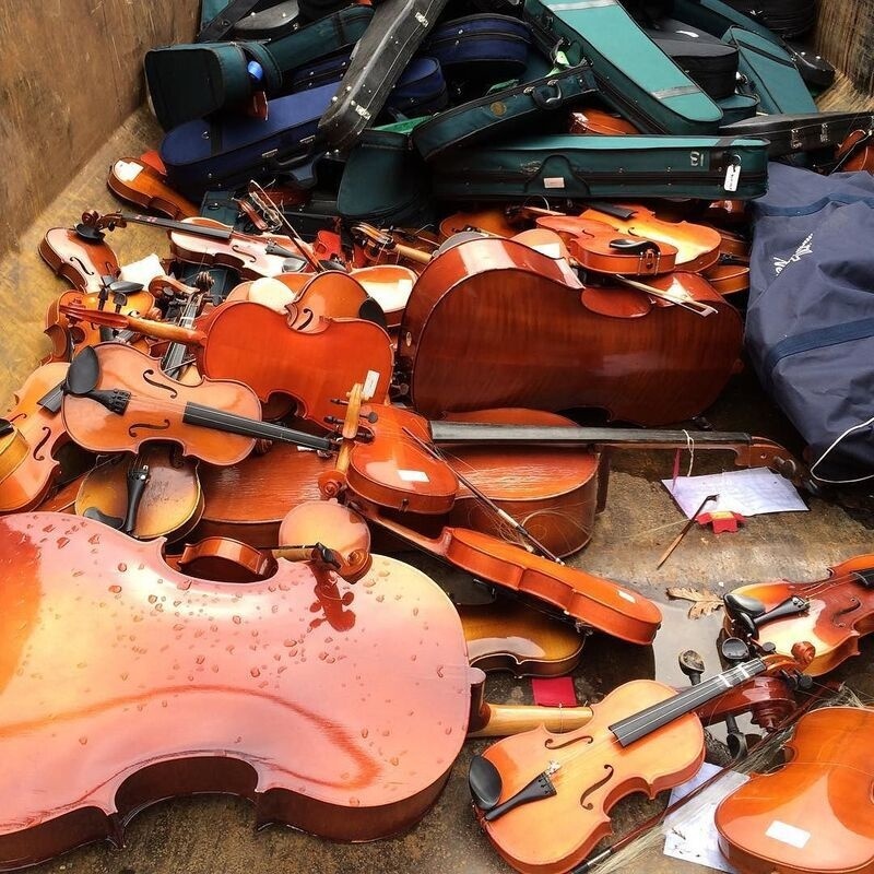 A pile of violins and their cases are scattered on the ground in a disorganized manner.