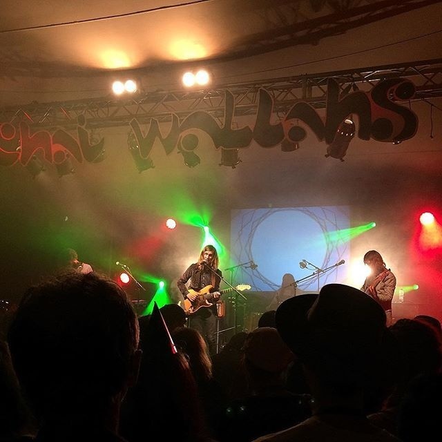 A live band performs on stage with colorful lights and an audience watching.