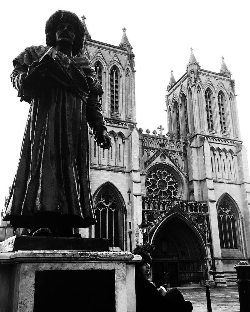 A statue stands prominently in front of a Gothic-style cathedral with large arched windows and tall towers.