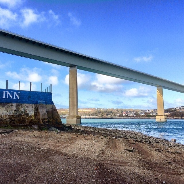 A large bridge spans across a body of water with a rocky shoreline and a partially visible building labeled INN on one side.