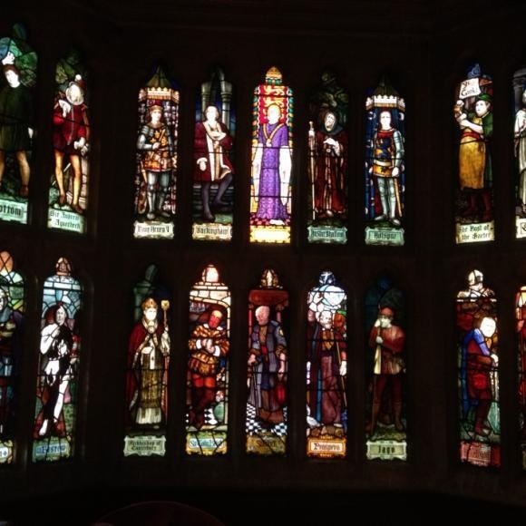 A series of stained glass windows depict various historical or religious figures in colorful robes and attire.