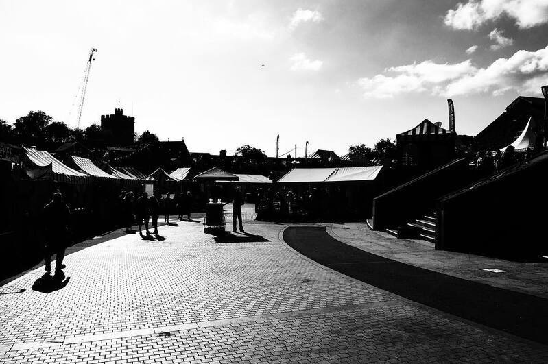 A marketplace with tents and people walking around is set against a bright sky with some clouds.