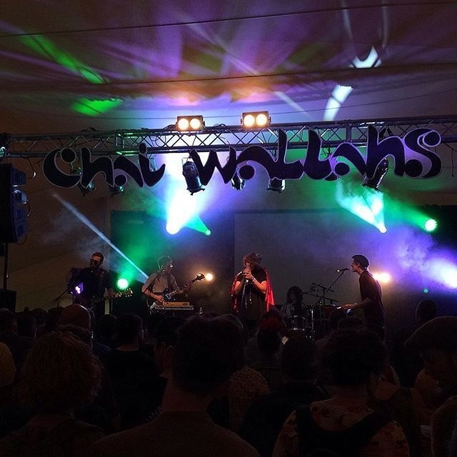A band is performing live on stage under colorful lights with an audience watching.
