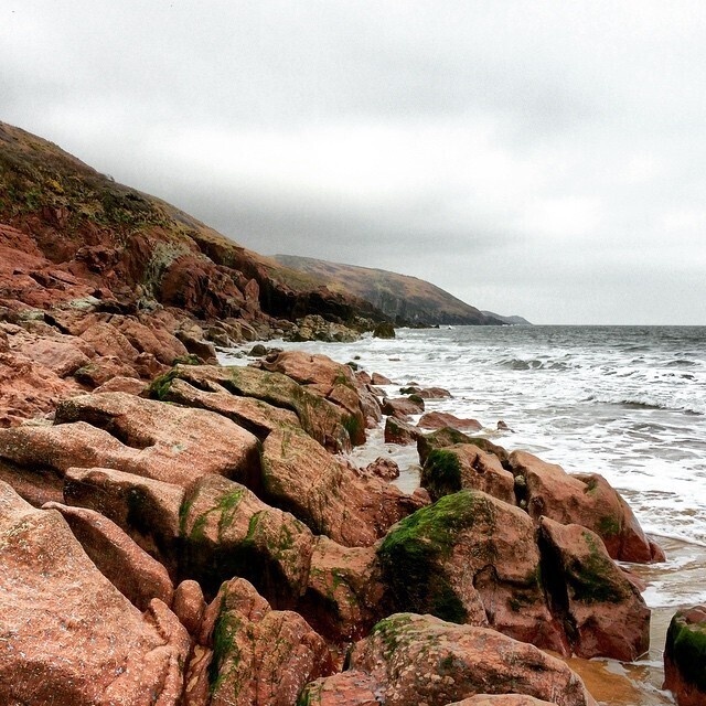 A rocky shoreline covered in patches of green moss stretches alongside a cloudy, choppy sea.