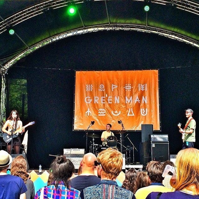 A band is performing on stage at the Green Man festival, with an audience watching in the foreground.