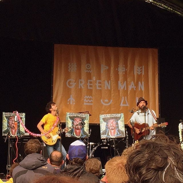 Two musicians are performing on stage in front of a crowd at the Green Man music festival.