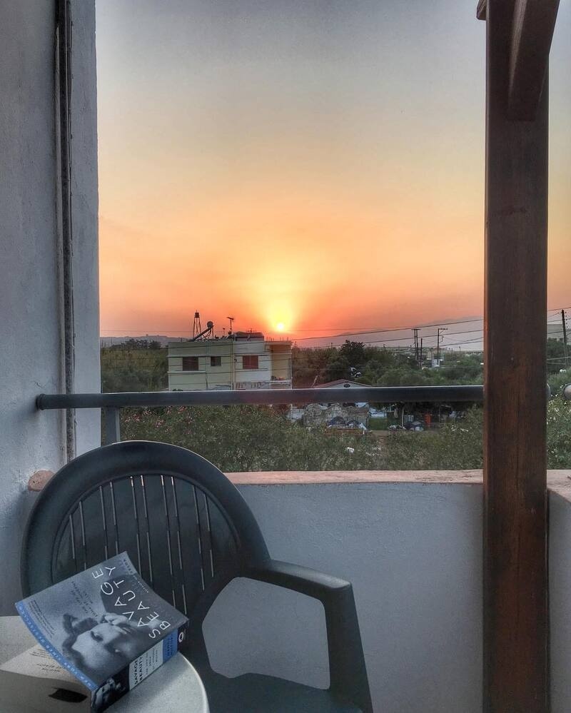 A serene balcony view with a chair, a book, and a vibrant sunset in the background.