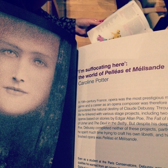 A person is holding and reading a book open to a page titled 'I'm suffocating here': the world of Pelléas et Mélisande by Caroline Potter, accompanied by a black-and-white portrait of a woman's face.