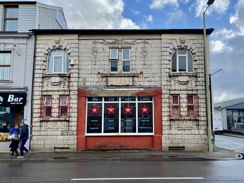 Exterior of ornate building with sign in window reading We Fix All Cars