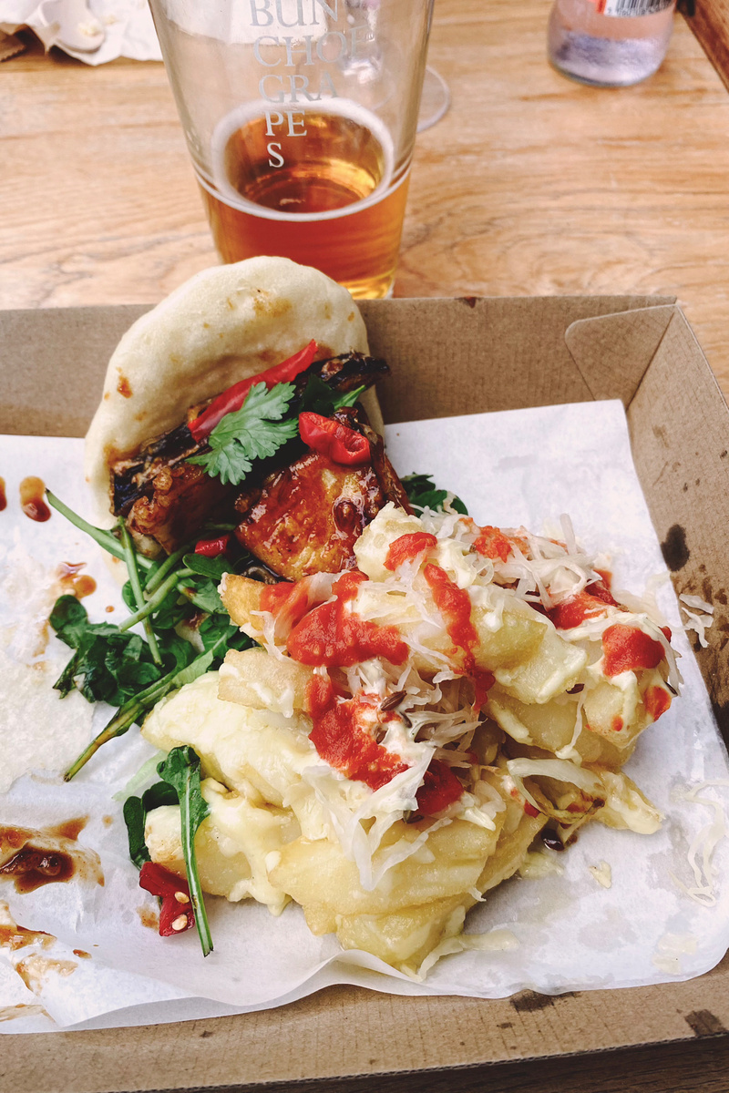 Messy platter of chips covered in sauce and fried aubergine in a bun with chillis and coriander