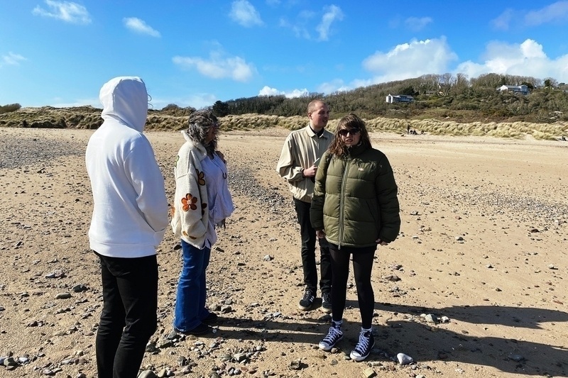 Four people looking windswept on a beach
