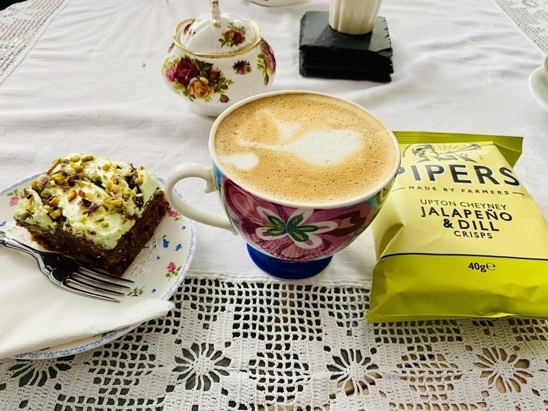 Piece of cake, packet of jalapeño & dill crisps and cup of coffee on a tablecloth