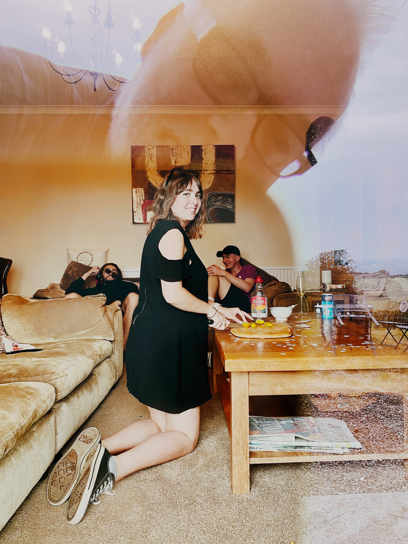 View through a window of woman cutting limes next to a tequila bottle, reflection in the window of a man watching what is happening