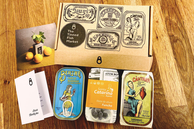 Three colour tinned fish tins of mackerel, tuna and sardines next to illustrated cardboard packaging