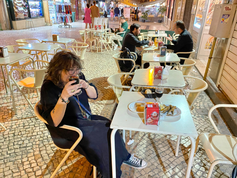 Woman seated at table of food and drink, two men at similar table in background