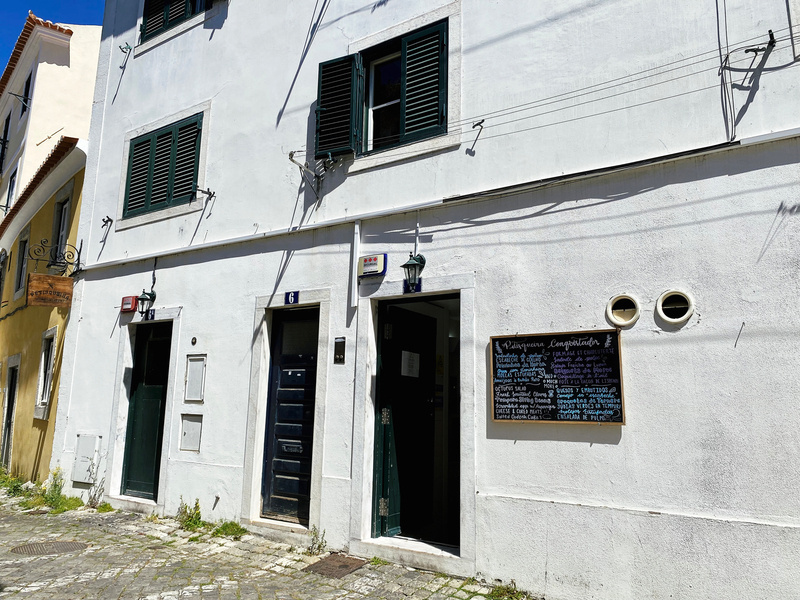 Exterior of a small white painted cafe, painted black doors and menu blackboard