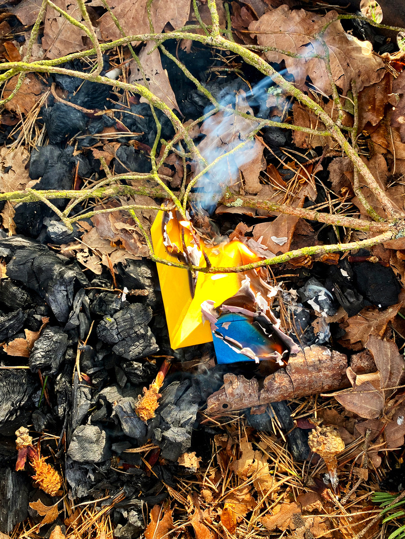 Folded coloured paper burning on a bed of dead leaves and charcoal