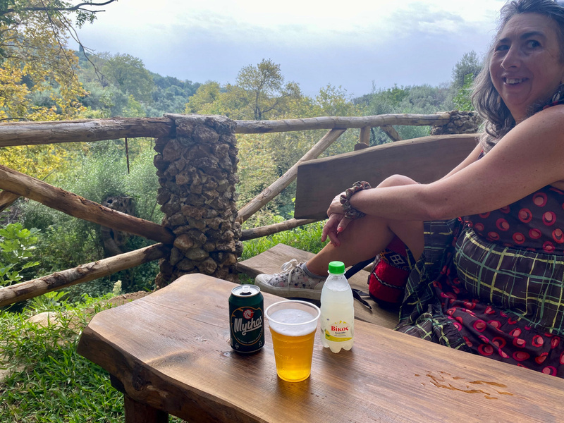 Woman sitting by table with beer and lemonade, view across tree covered hills