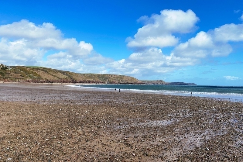Almost deserted beach, tide out, expanse of stony sand and cloudy blue sky