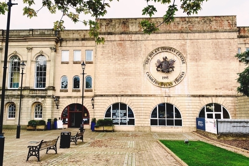 Beige blocky building with arched windows and large coat of arms mounted on front wall.