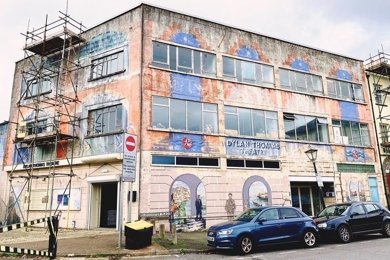 Three storey building with some scaffolding. Colourfully painted but faded and needing redocoration and repair