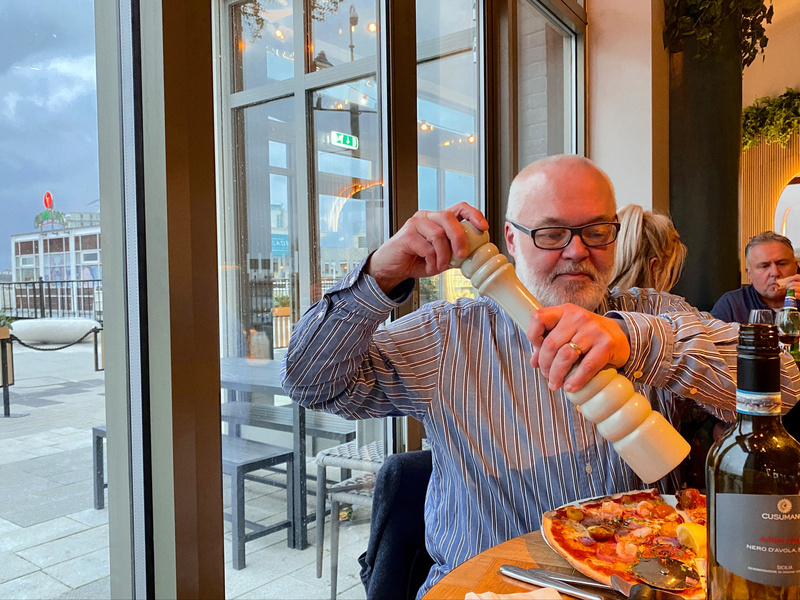 Man using very large pepper grinder over a pizza