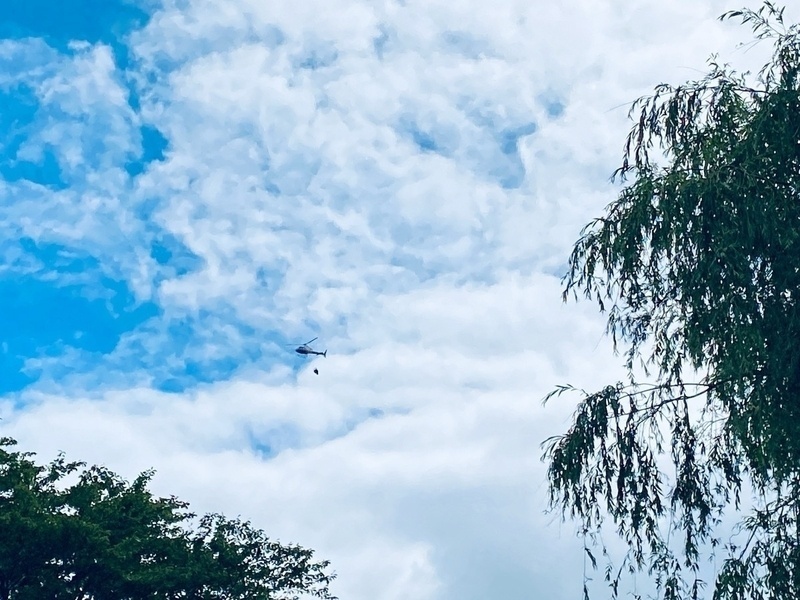 Distant view of helicopter in the sky, fire fighting water container slung beneath it
