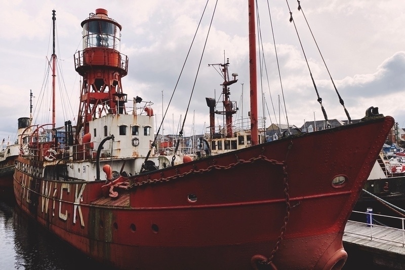 Rusting orange and white ship with central iron tower supporting a large glass light enclosure at its top