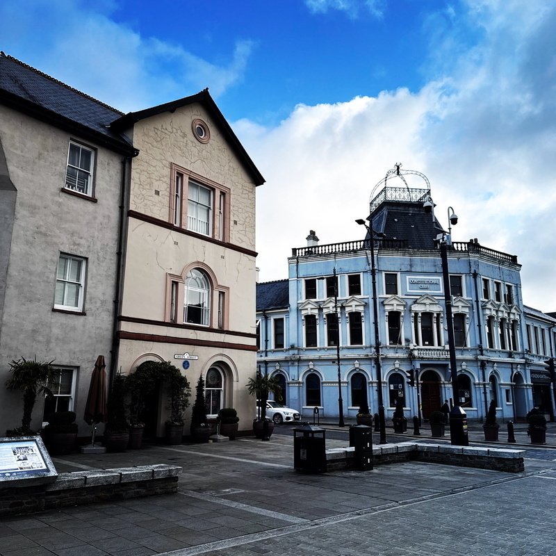 Auto-generated description: Two historic buildings with distinct architectural styles are set against a partly cloudy sky.