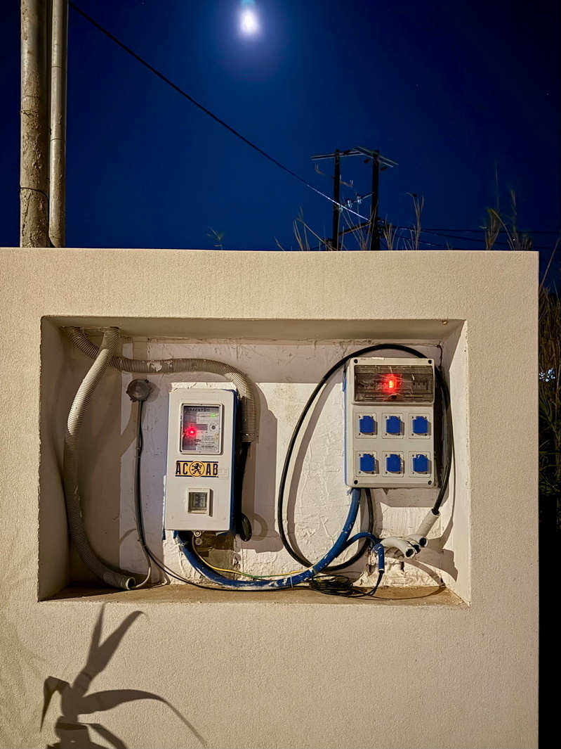 Auto-generated description: Two electrical boxes with wires are mounted on a white wall under a night sky with a visible moon.