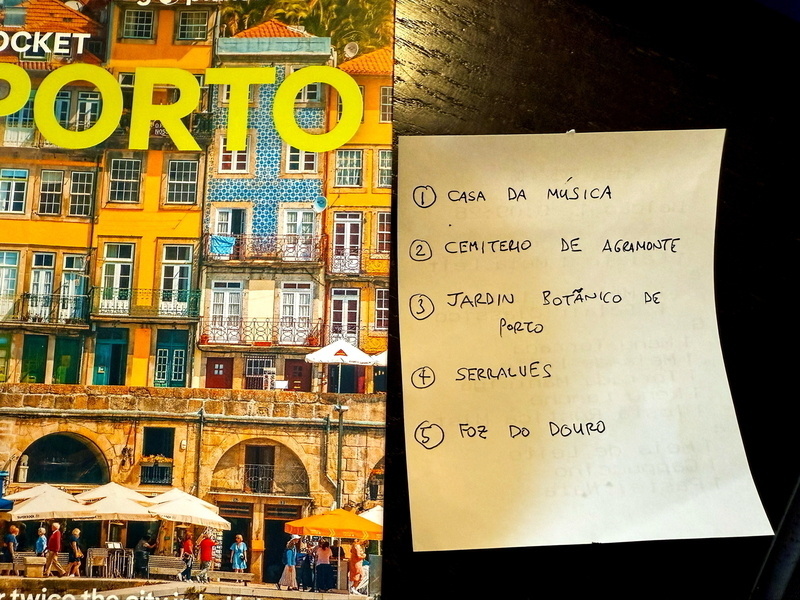 Auto-generated description: A travel guidebook for Porto is beside a handwritten list of five places to visit in the city.