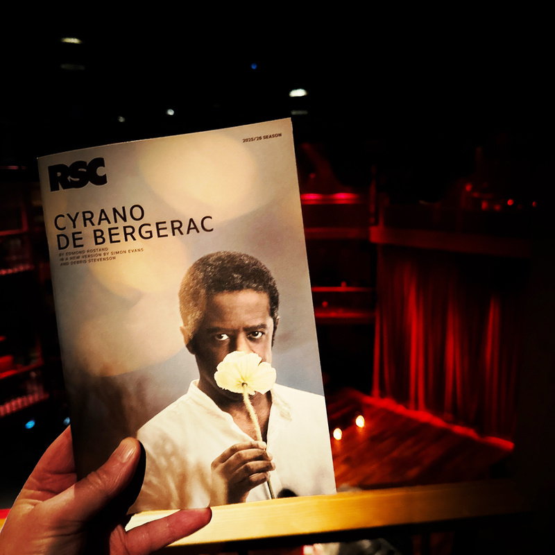 Auto-generated description: A person holds up a program for Cyrano de Bergerac by the Royal Shakespeare Company at a theater.