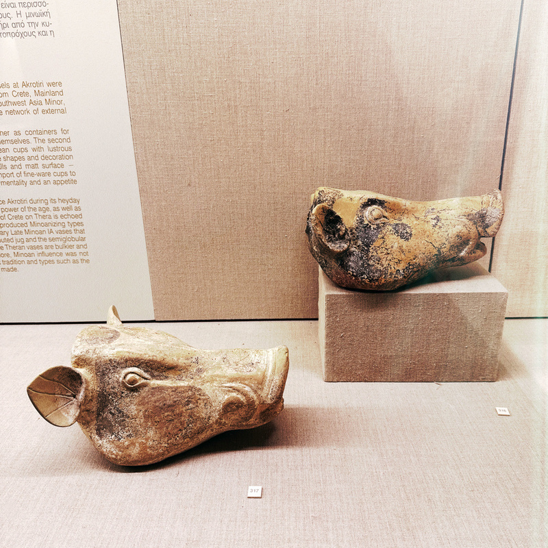 Two ancient, intricately carved animal head sculptures are displayed on pedestals against a backdrop with text.
