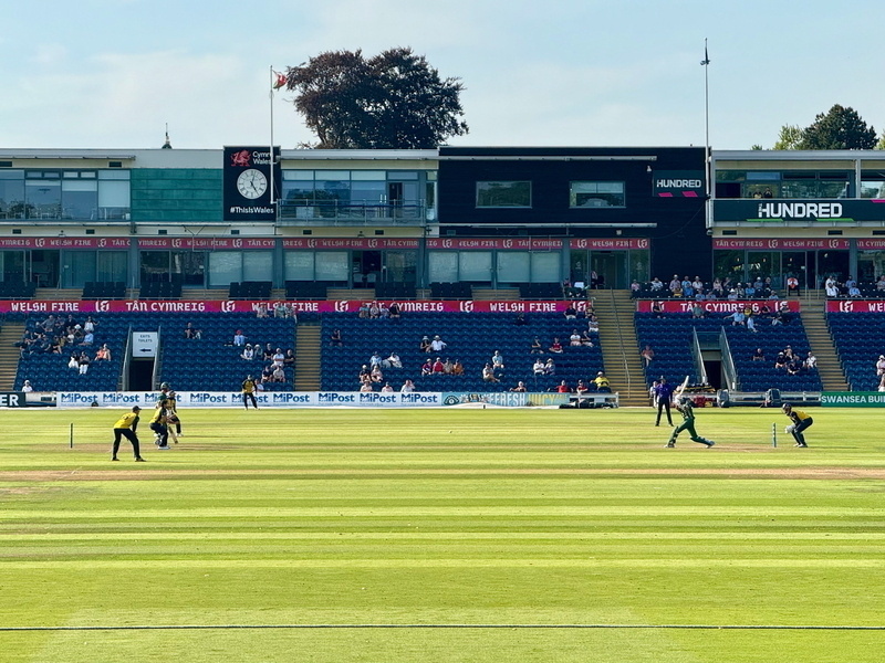 Auto-generated description: A cricket match is taking place in a stadium with spectators watching from the stands.