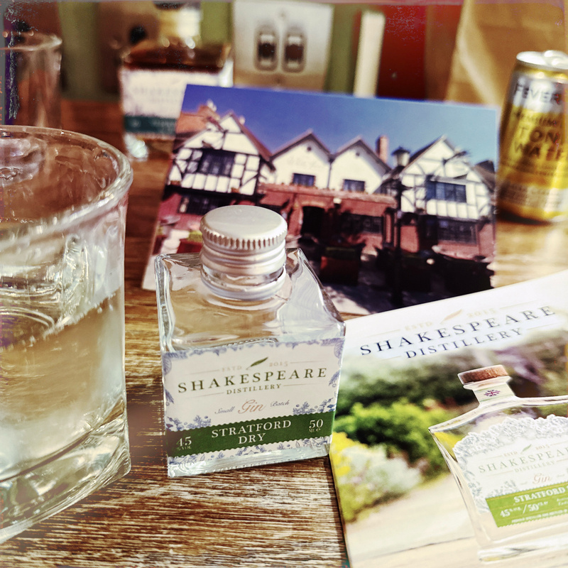 Auto-generated description: A small bottle of Stratford Dry gin is surrounded by a glass of gin and tonic and a card featuring a picture of a hotel.
