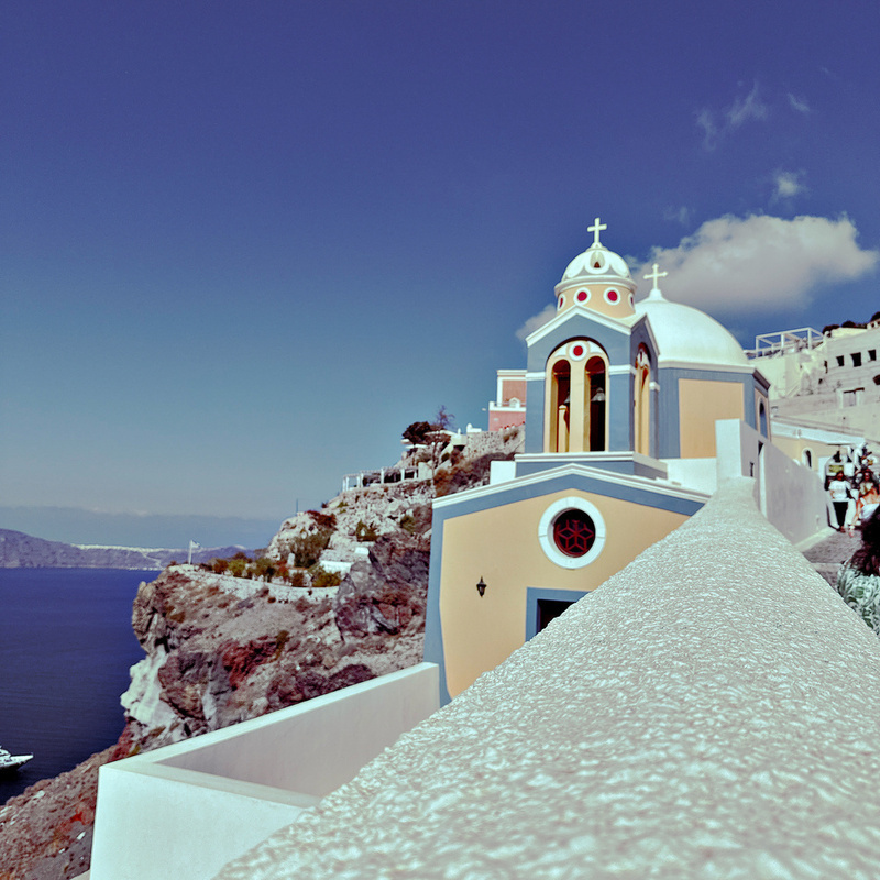 A picturesque coastal scene features a vibrant building with a dome set against a clear blue sky and sea background.