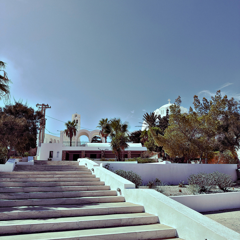A white building with arches is surrounded by palm trees and greenery under a clear blue sky.