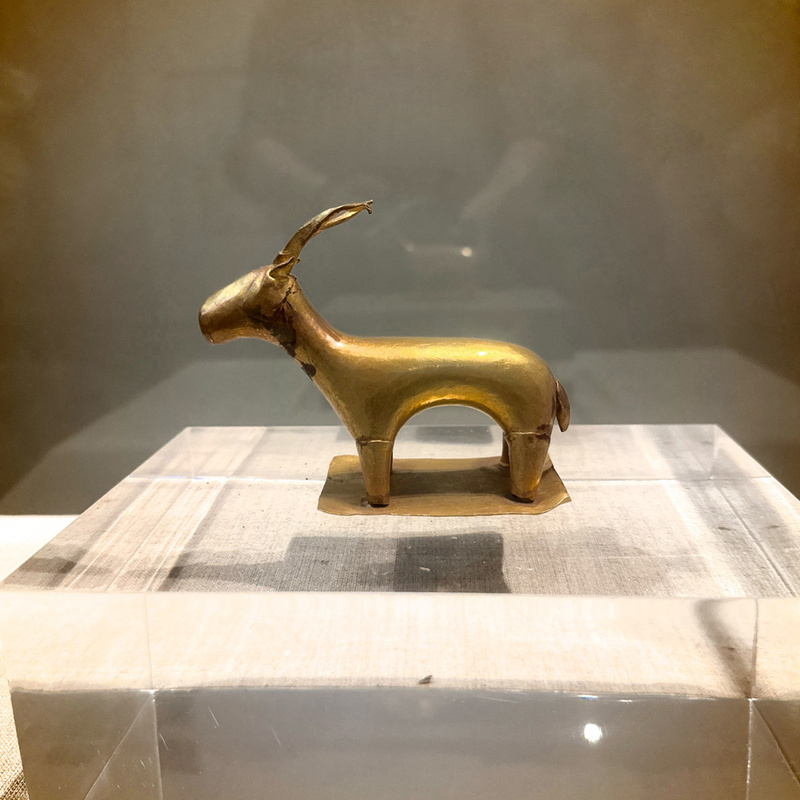 A small, gold-toned sculpture of an animal stands on display, encased within a clear protective box.