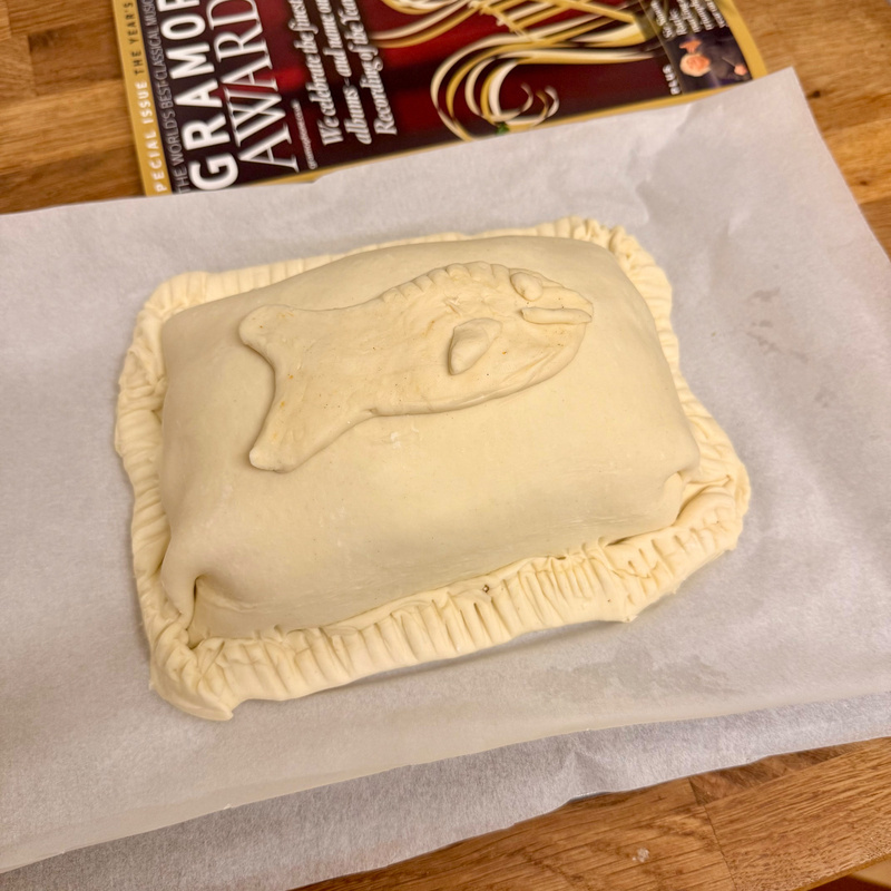 Auto-generated description: A rectangular pastry with crimped edges and a fish-shaped design on top rests on parchment paper.
