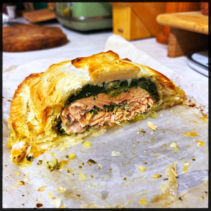 Auto-generated description: A cross-section of a baked pastry reveals a filling of salmon and greens.