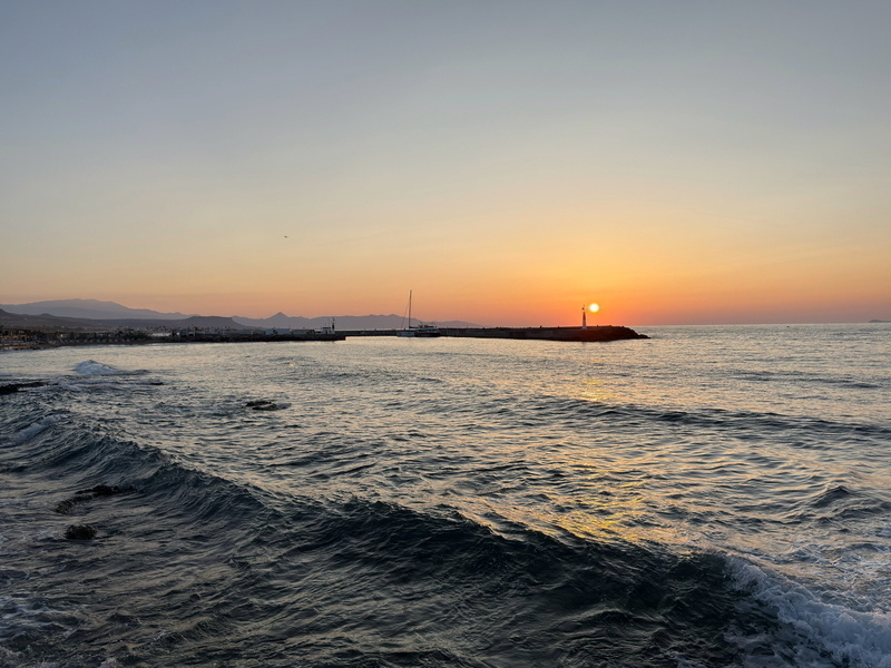 Auto-generated description: A tranquil sunset over the ocean with gentle waves and a distant sailboat near the horizon.