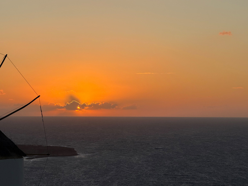 Auto-generated description: A serene sunset over the ocean with clouds partially covering the sun near the horizon.
