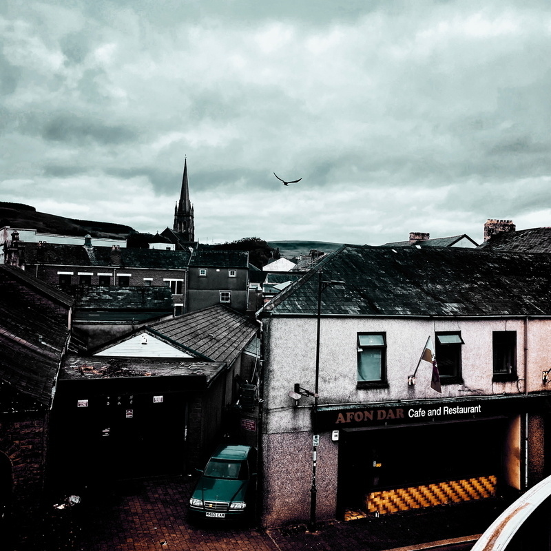A dramatic sky looms over a small town with a prominent church steeple and a building in the foreground labeled Afon Dar Café and Restaurant.