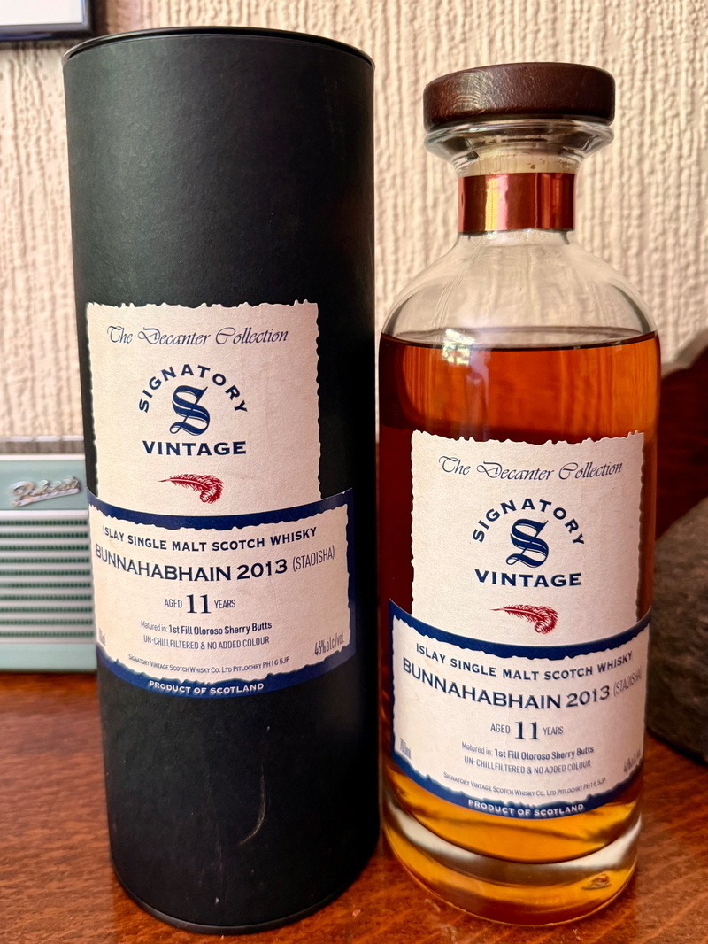 Auto-generated description: A bottle of Bunnahabhain 2013 Islay Single Malt Scotch Whisky aged 11 years is displayed alongside its cylindrical packaging.