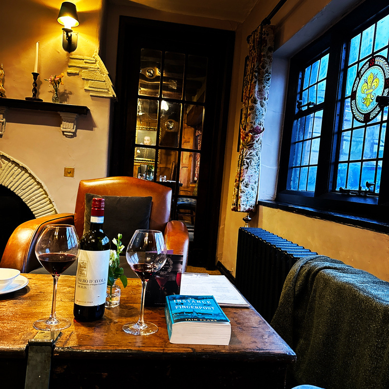 Auto-generated description: A cozy room features a fireplace with candles, a stained glass window, wine glasses on a wooden table, and comfortable armchairs.