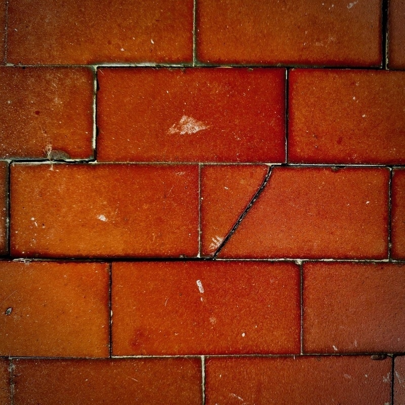Auto-generated description: Red brick tiles arranged in a rectangular pattern show wear and a crack in one of the tiles.