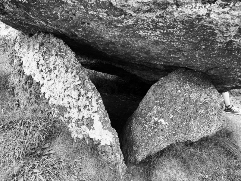 Auto-generated description: Two large rocks support a massive boulder, creating a small cave-like space underneath.